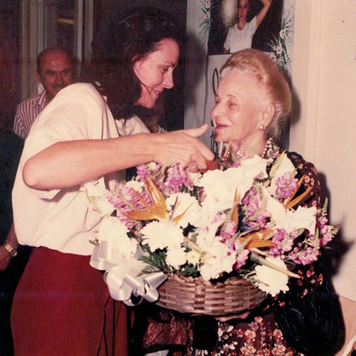 Sra. Maria recebendo flores da representante do Governador.